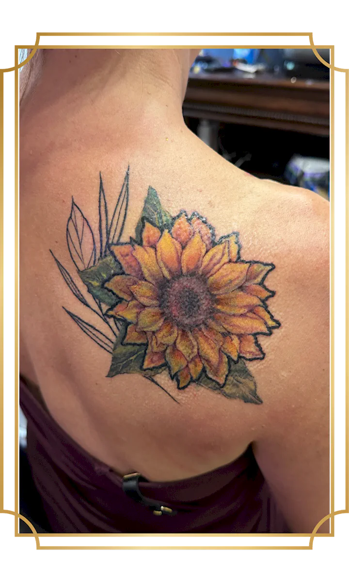 Color sunflower cover-up tattoo with orange and yellow petals, green leaves and botanical linework on the shoulder blade