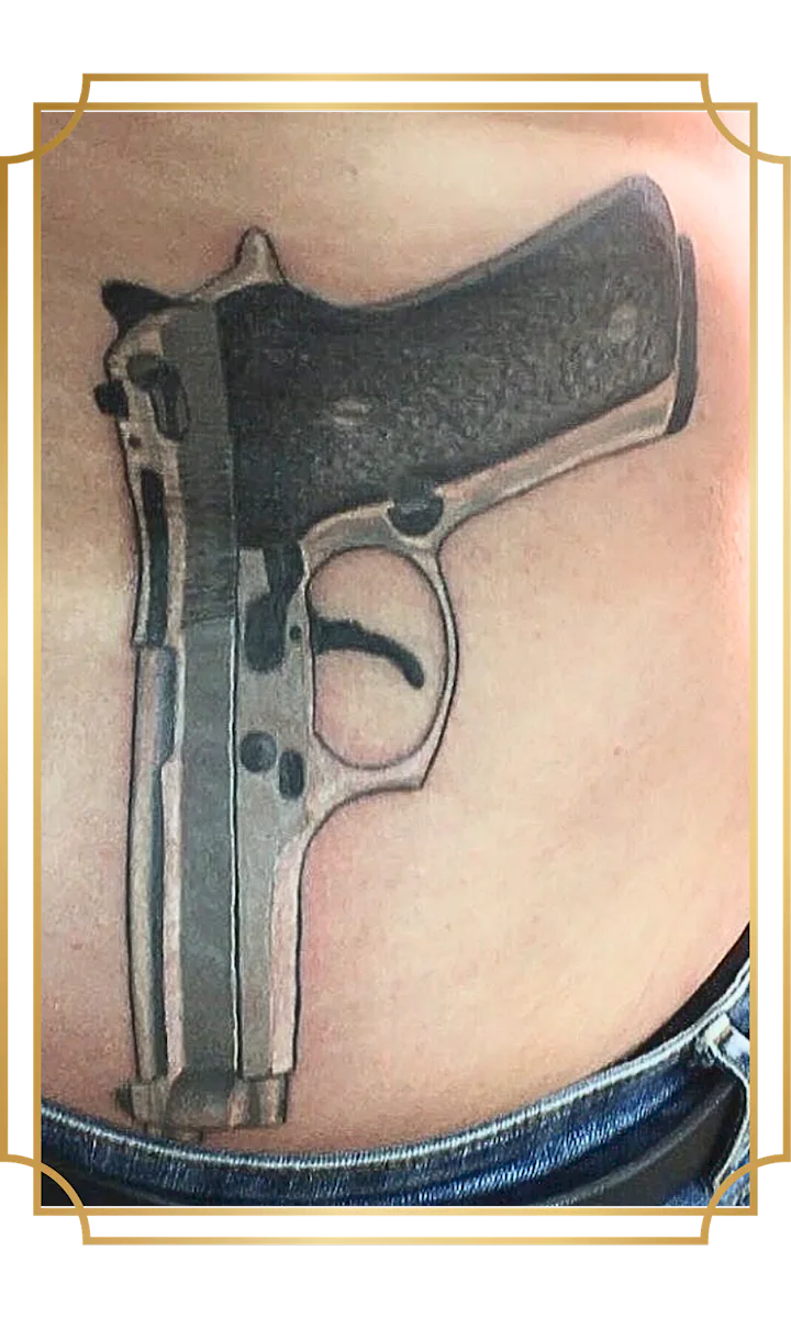 Black-and-gray realism pistol tattoo on the lower abdomen with a textured grip, metallic highlights and detailed mechanical features, created in San Marcos