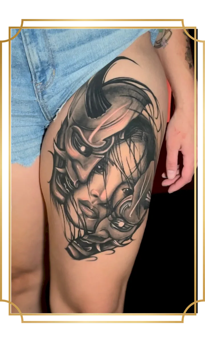Black and gray woman's face tattoo framed by Japanese armor and mask details on the thigh