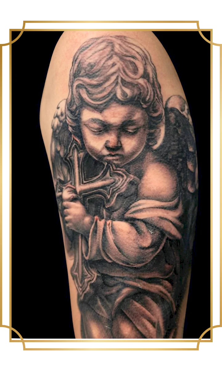 Black and gray cherub angel holding a cross tattoo on the arm