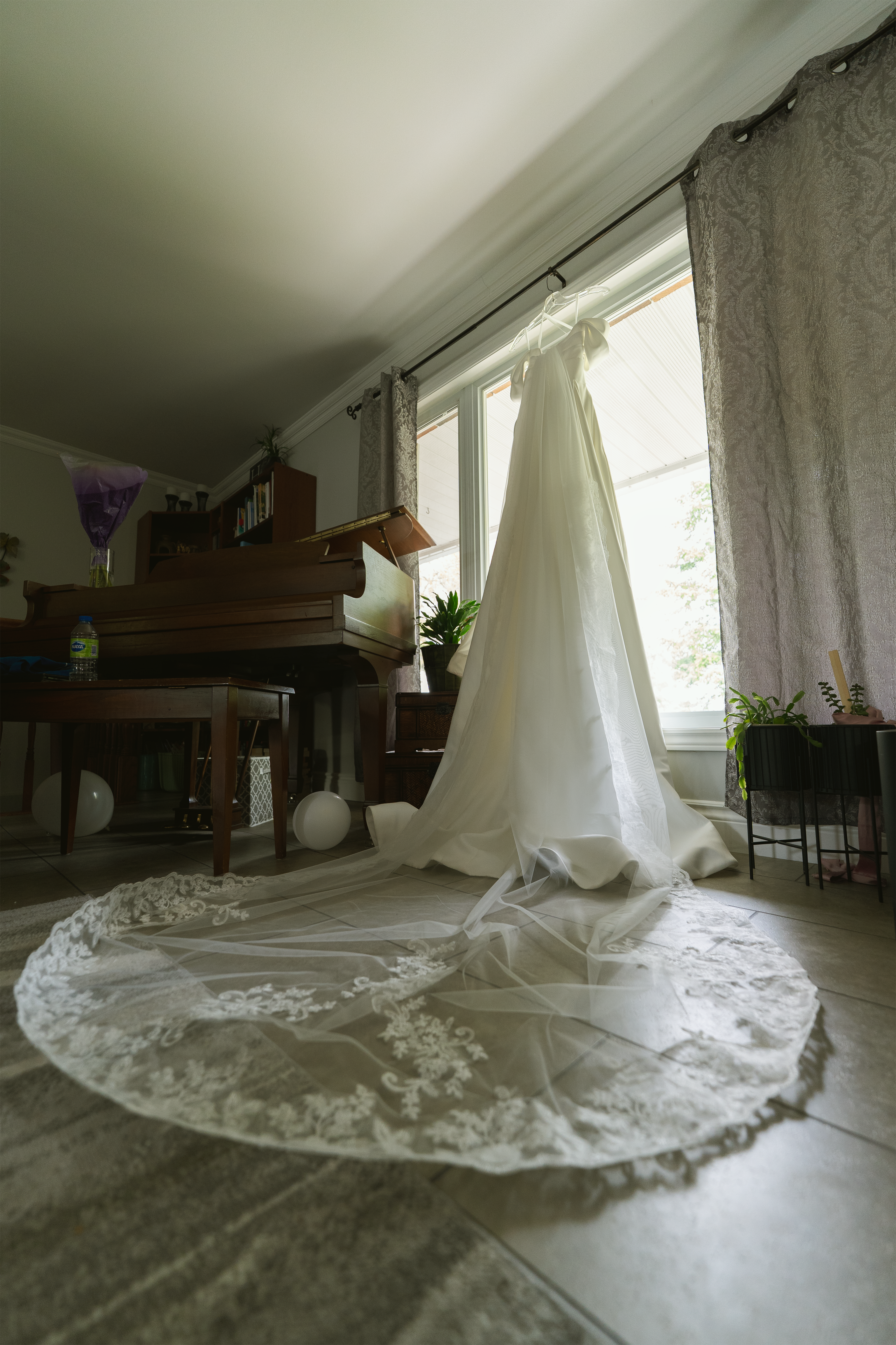 White wedding gown with a long lace train hanging by a window before the ceremony.