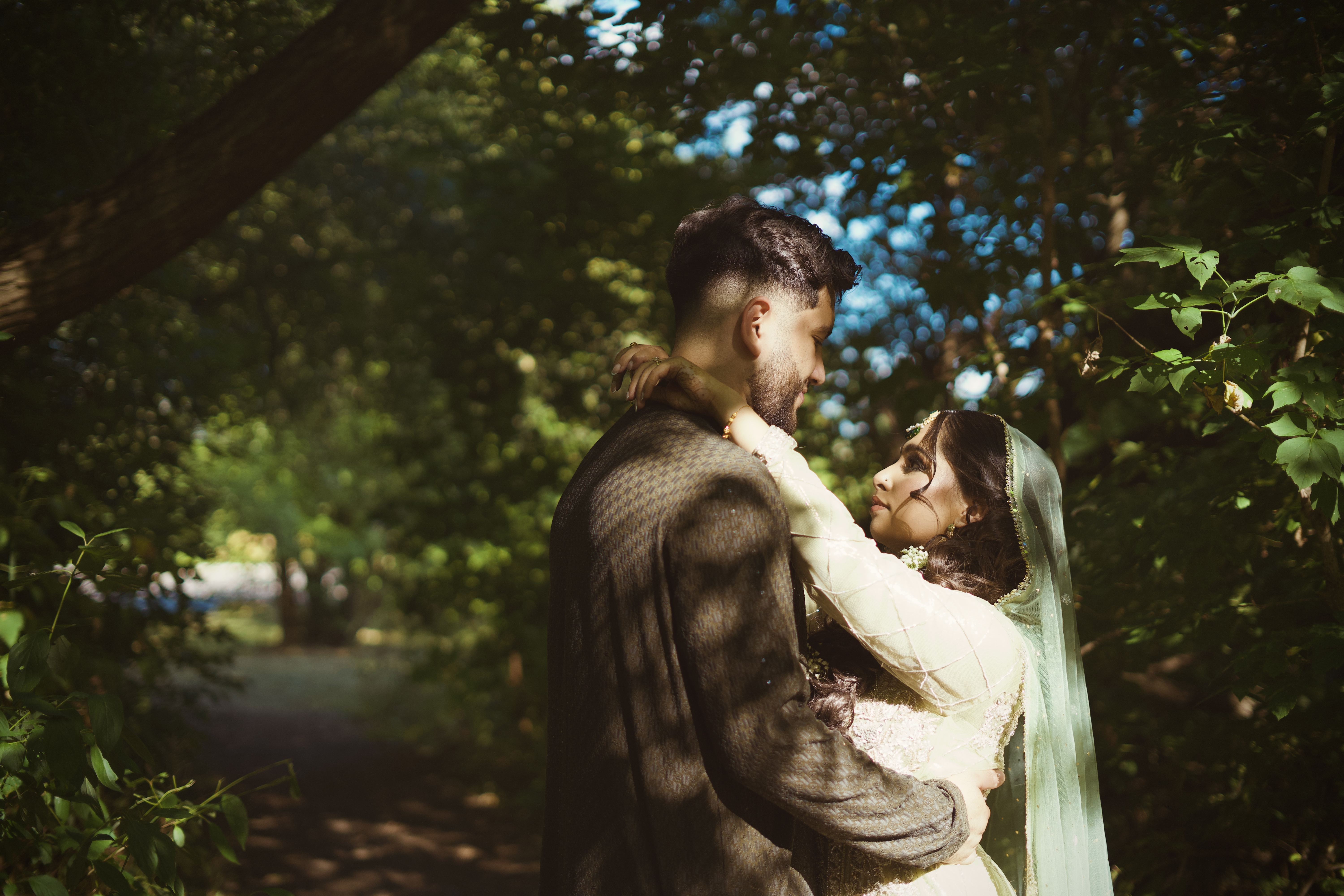 Bride in a cream outfit and mint dupatta embracing her groom in a sunlit forest.