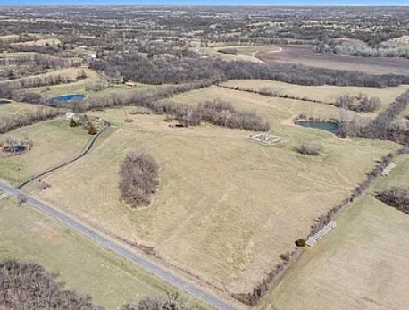 Road-level aerial of 18211 Plattsburg Road showing county road frontage and open pasture