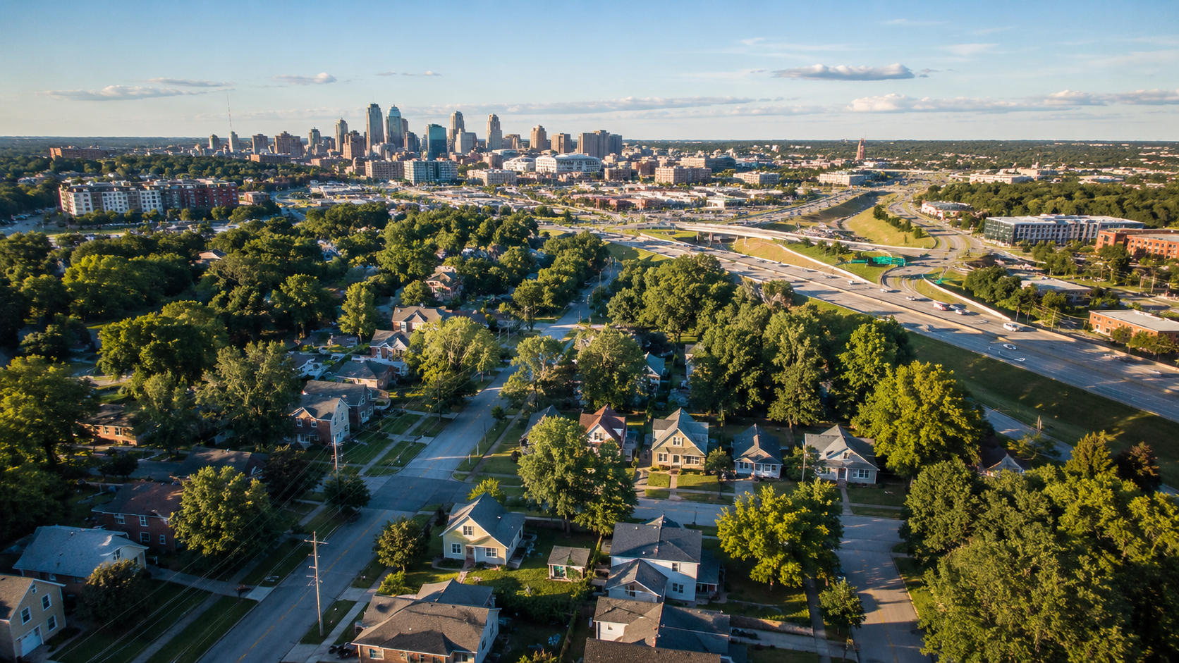 Aerial view of an established Kansas City neighborhood with mature trees, nearby highway access and the downtown skyline in the distance.