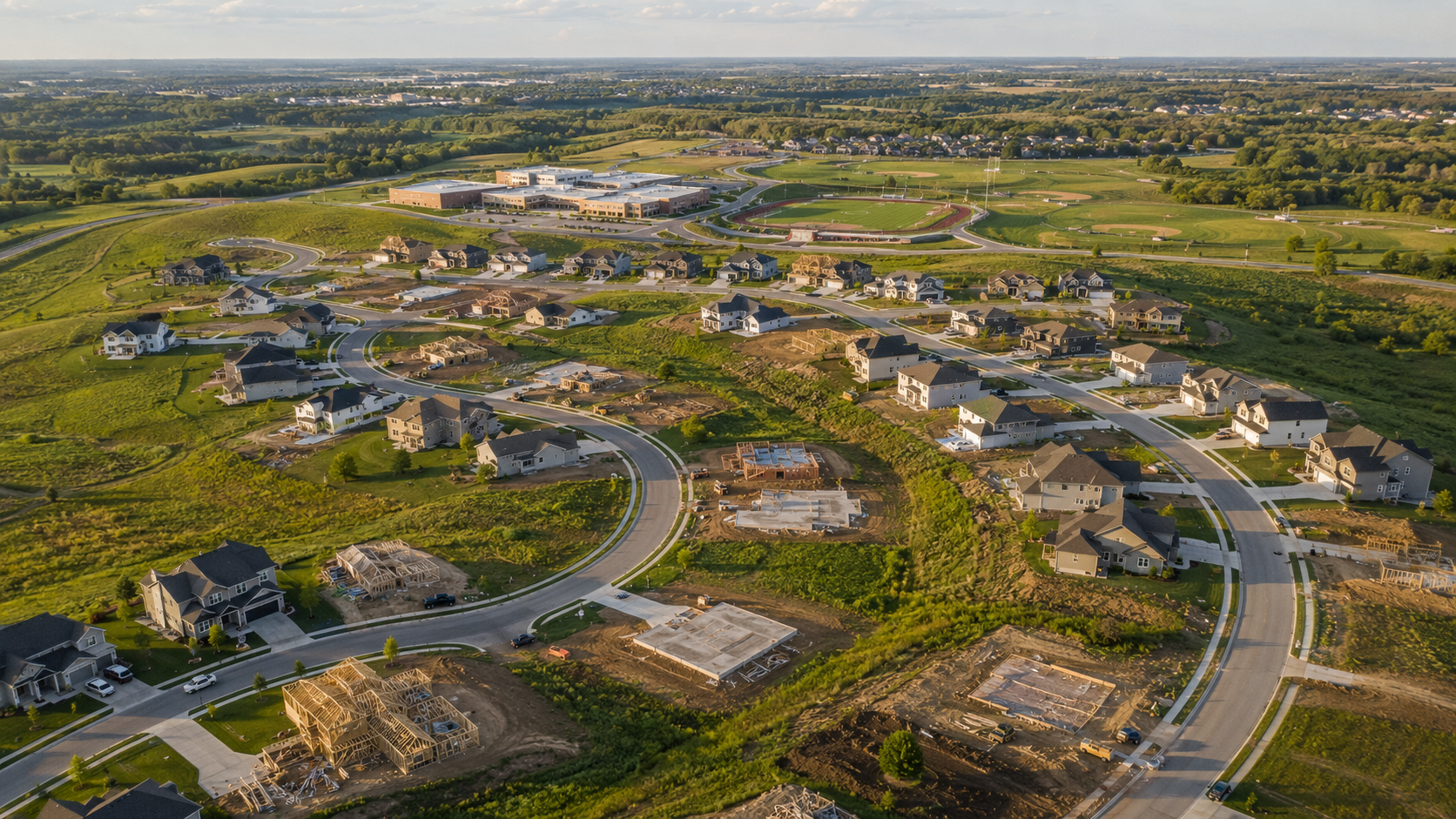 Aerial view of a growing Kansas City Northland subdivision with new homes, construction sites, and nearby schools and sports fields.