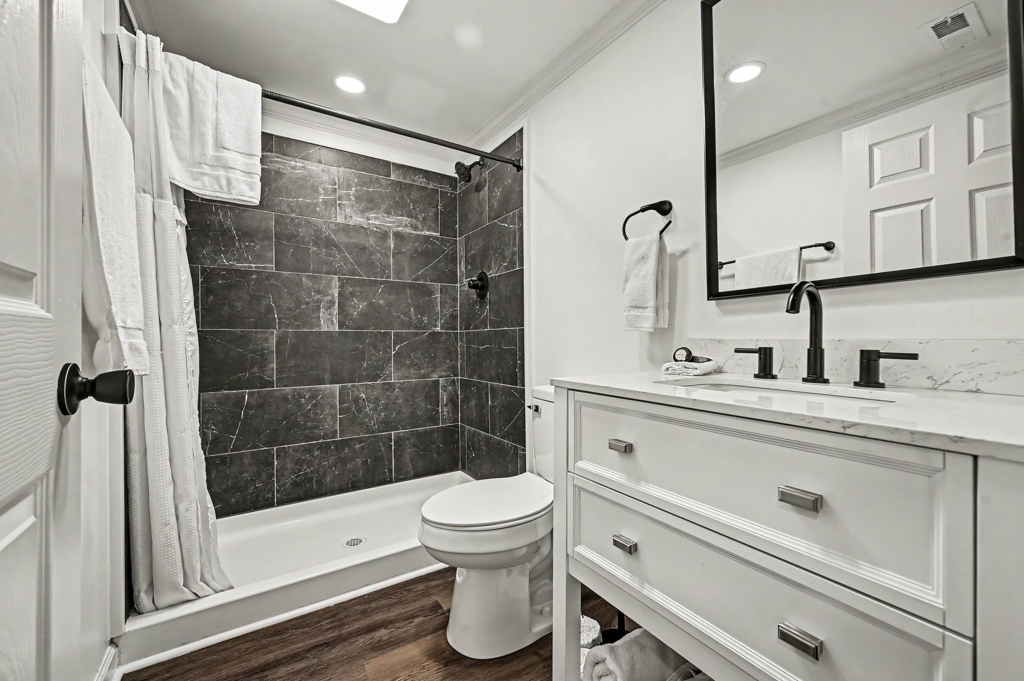 Bathroom with charcoal marble-look tiled shower, white vanity and matte black faucet