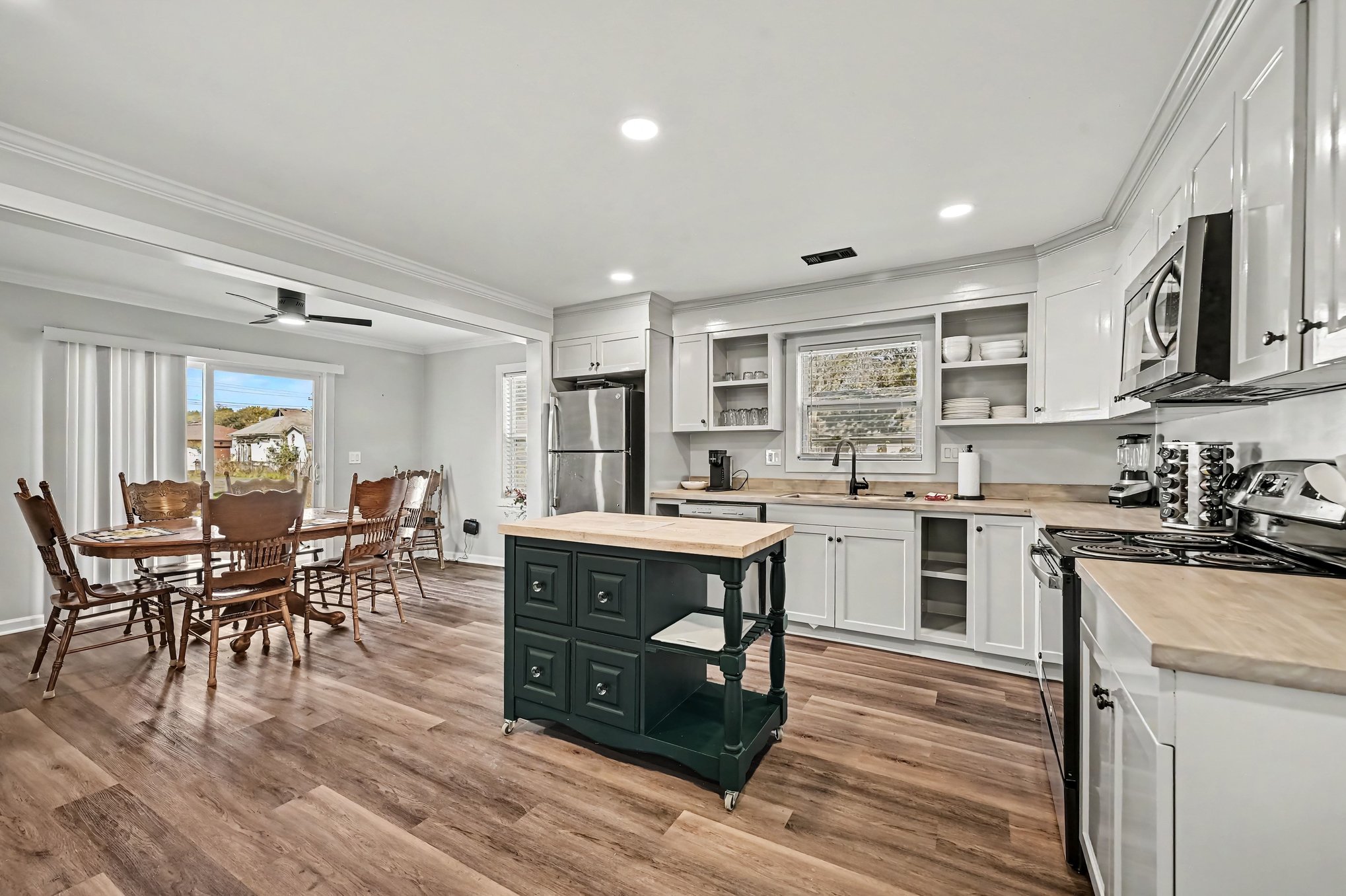 Renovated kitchen with white shaker cabinets, butcher-block island, stainless steel refrigerator and microwave, open to dining area