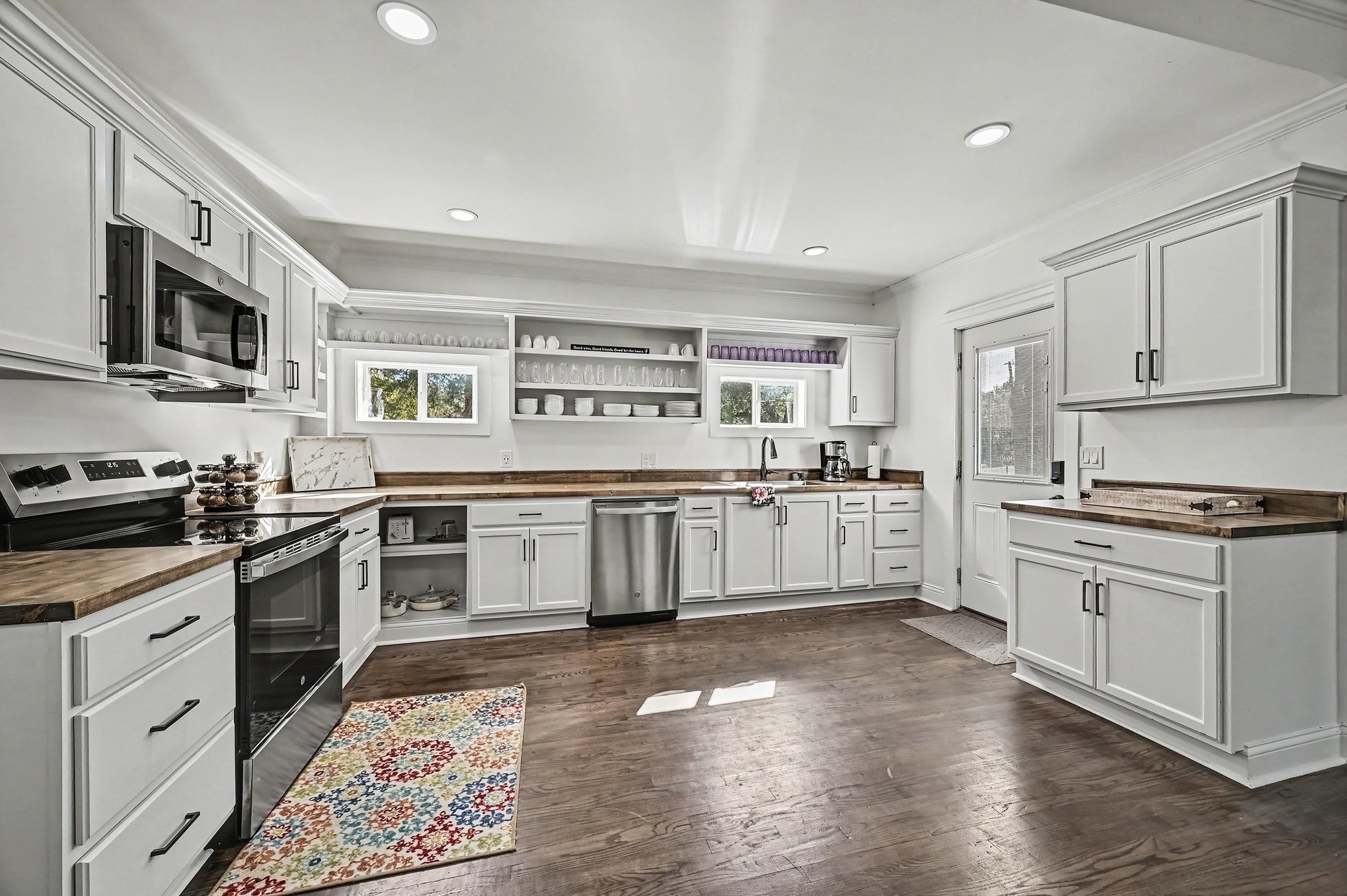 Main house kitchen with white shaker cabinets, butcher-block counters, open shelving and stainless steel appliances