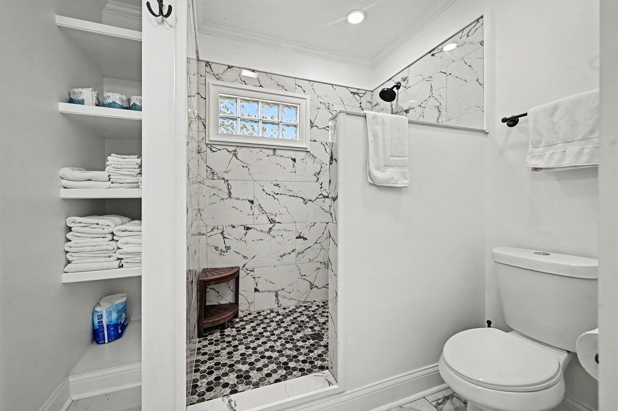 Main-level walk-in shower with marble-look tile, hexagon mosaic floor and built-in linen shelves