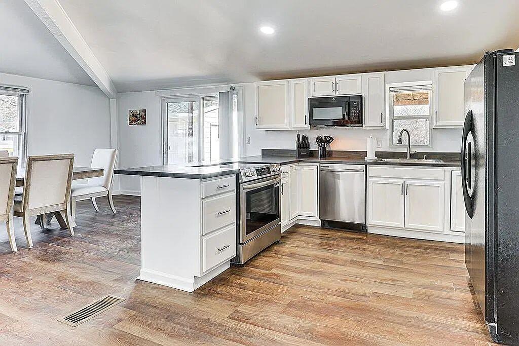 Updated kitchen with white shaker cabinets, peninsula, stainless range and dishwasher, open to dining area with sliding glass door