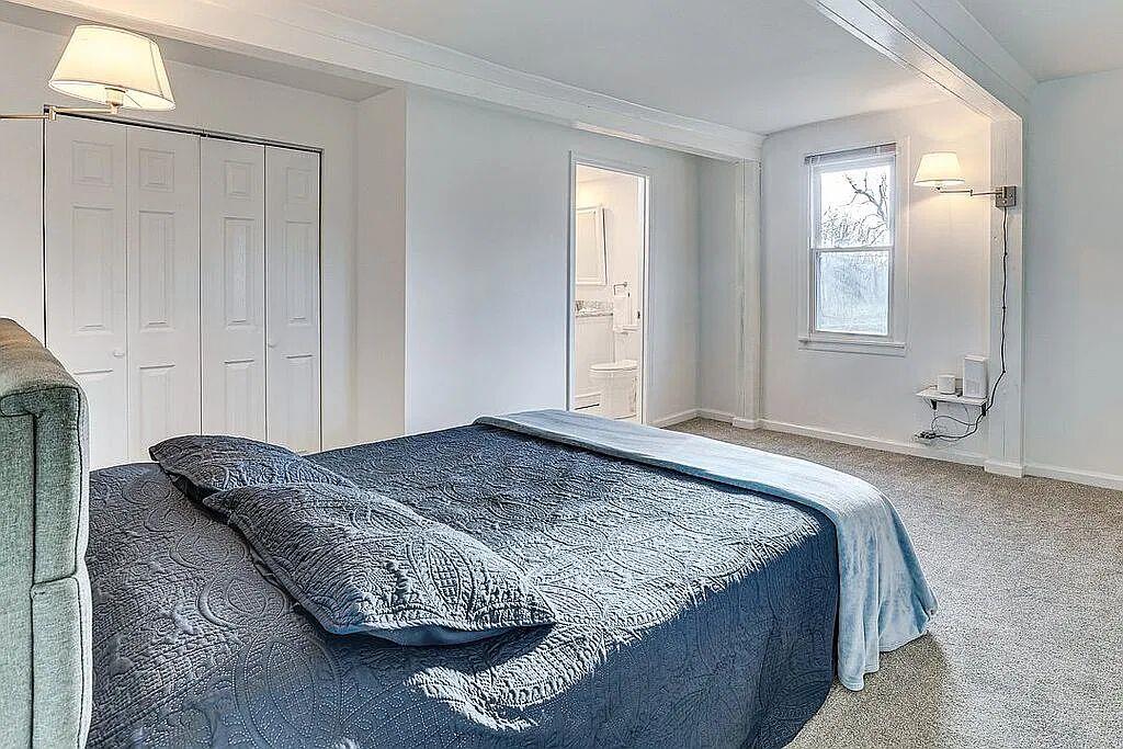 Primary bedroom with carpet, double closet, swing-arm sconces and adjoining bathroom
