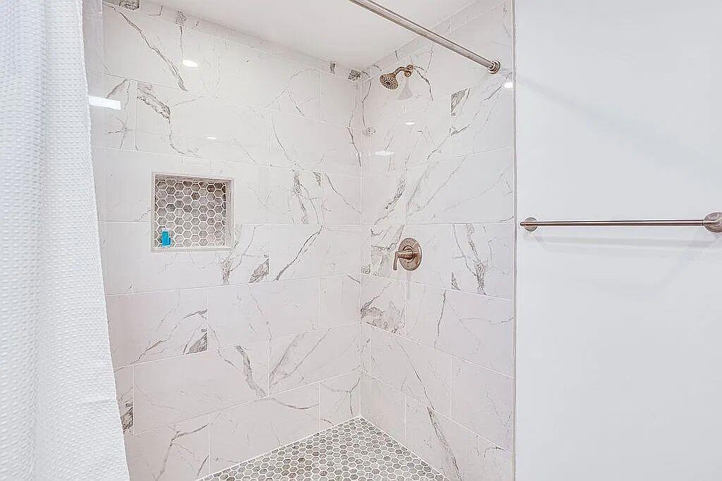 Walk-in shower with marble-look tile, hexagon mosaic floor and recessed niche