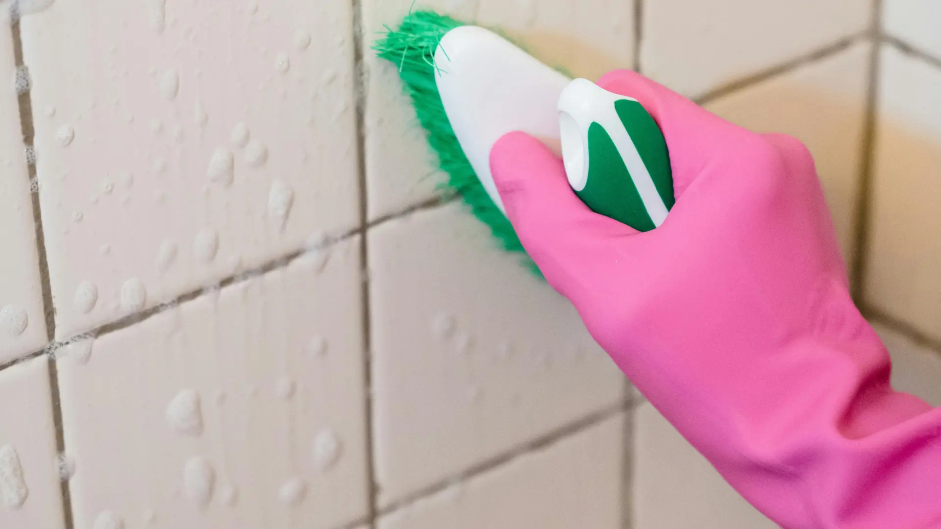 alt="A Crisp Clean Home professional in a pink glove meticulously scrubbing white tile and grout in a Maryland bathroom."