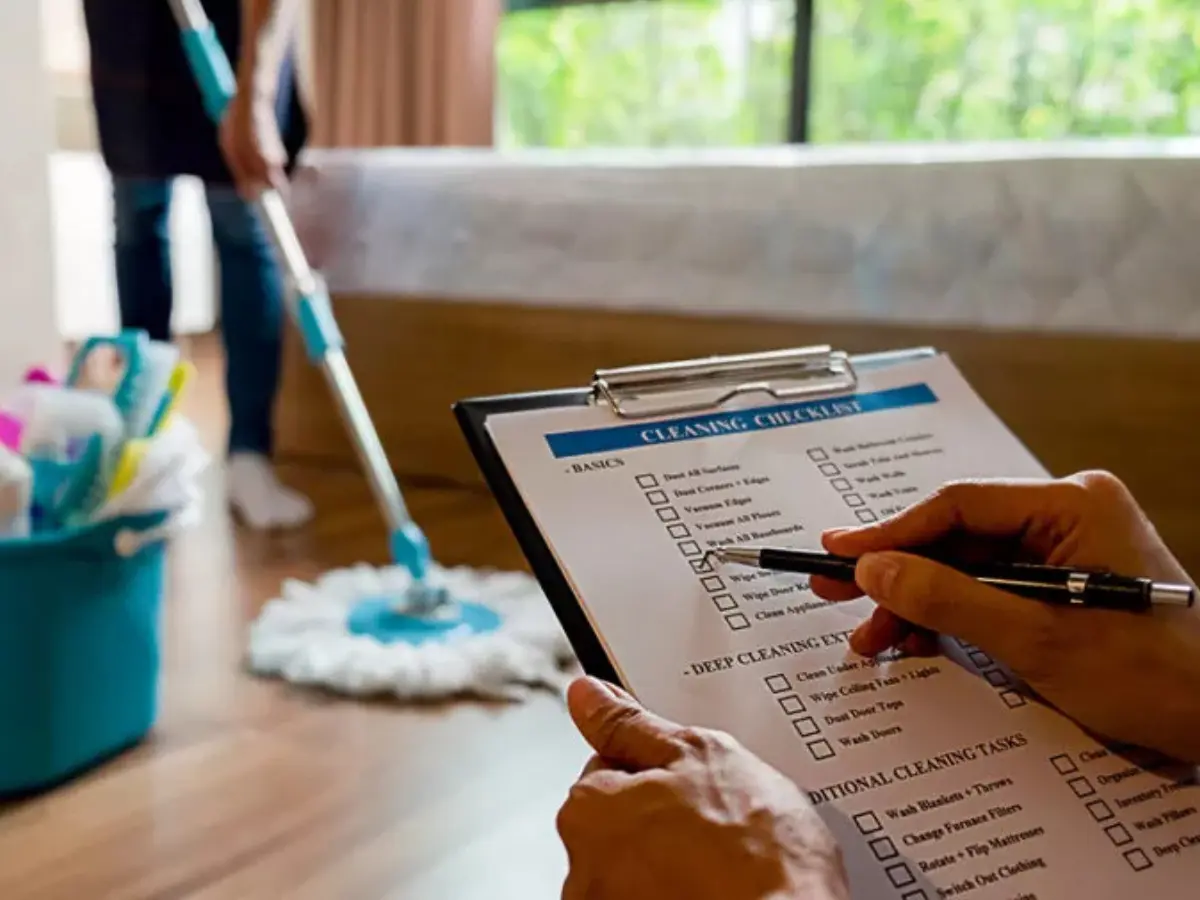 alt="A supervisor with a checklist inspects a professional cleaner who is dry mopping hardwood floors during a move-out clean in Maryland."