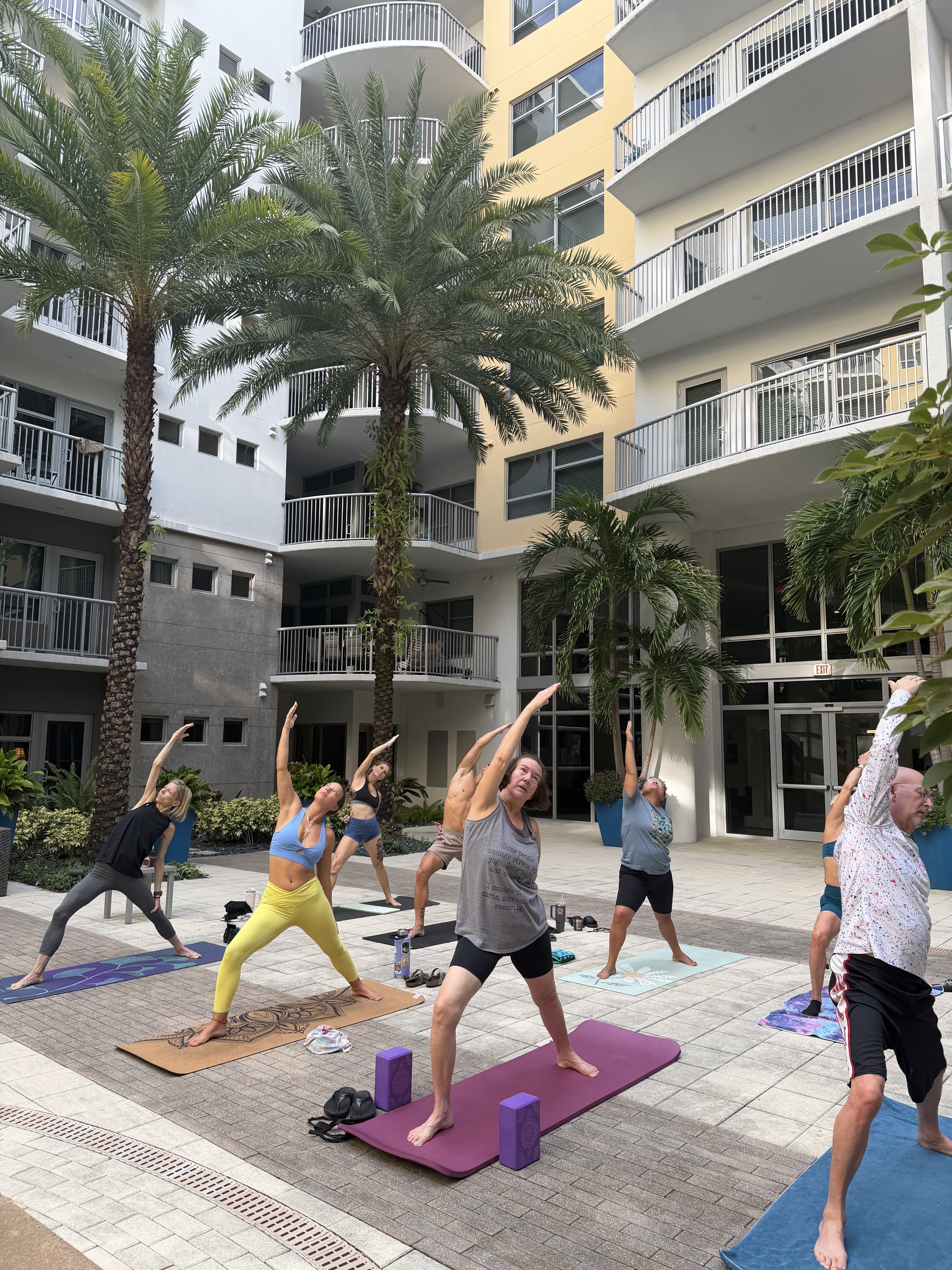 Jenny leading a group yoga class in a palm-lined courtyard