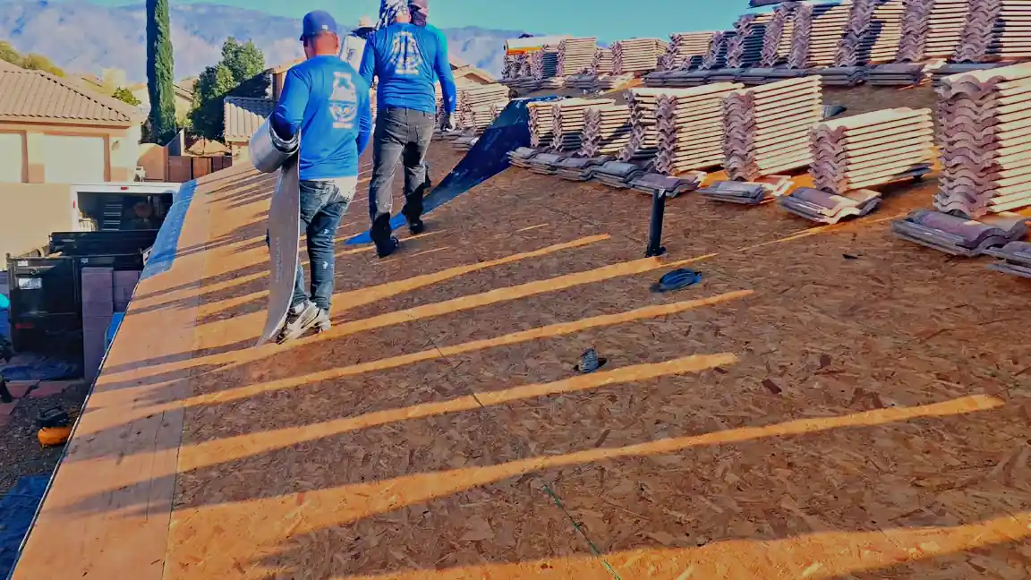 Crew carrying underlayment across a stripped deck, tile staged behind