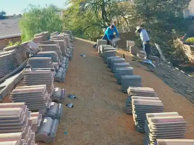 Tile stacked in rows on a stripped roof deck, crew working behind