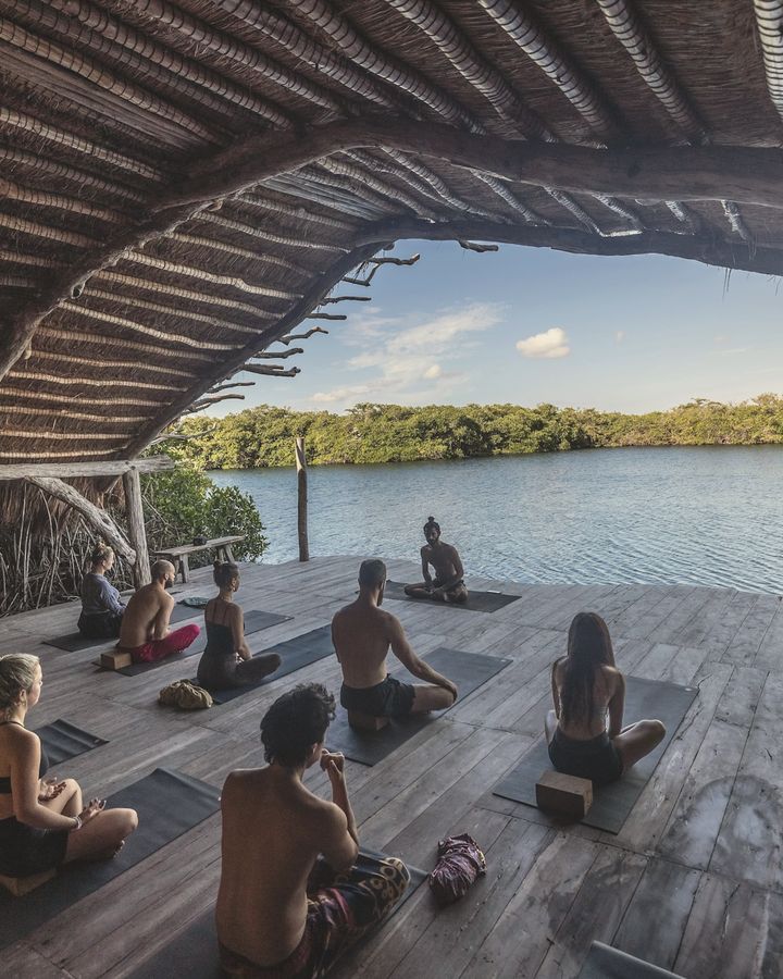 A group practicing yoga on a covered wooden deck above a lake