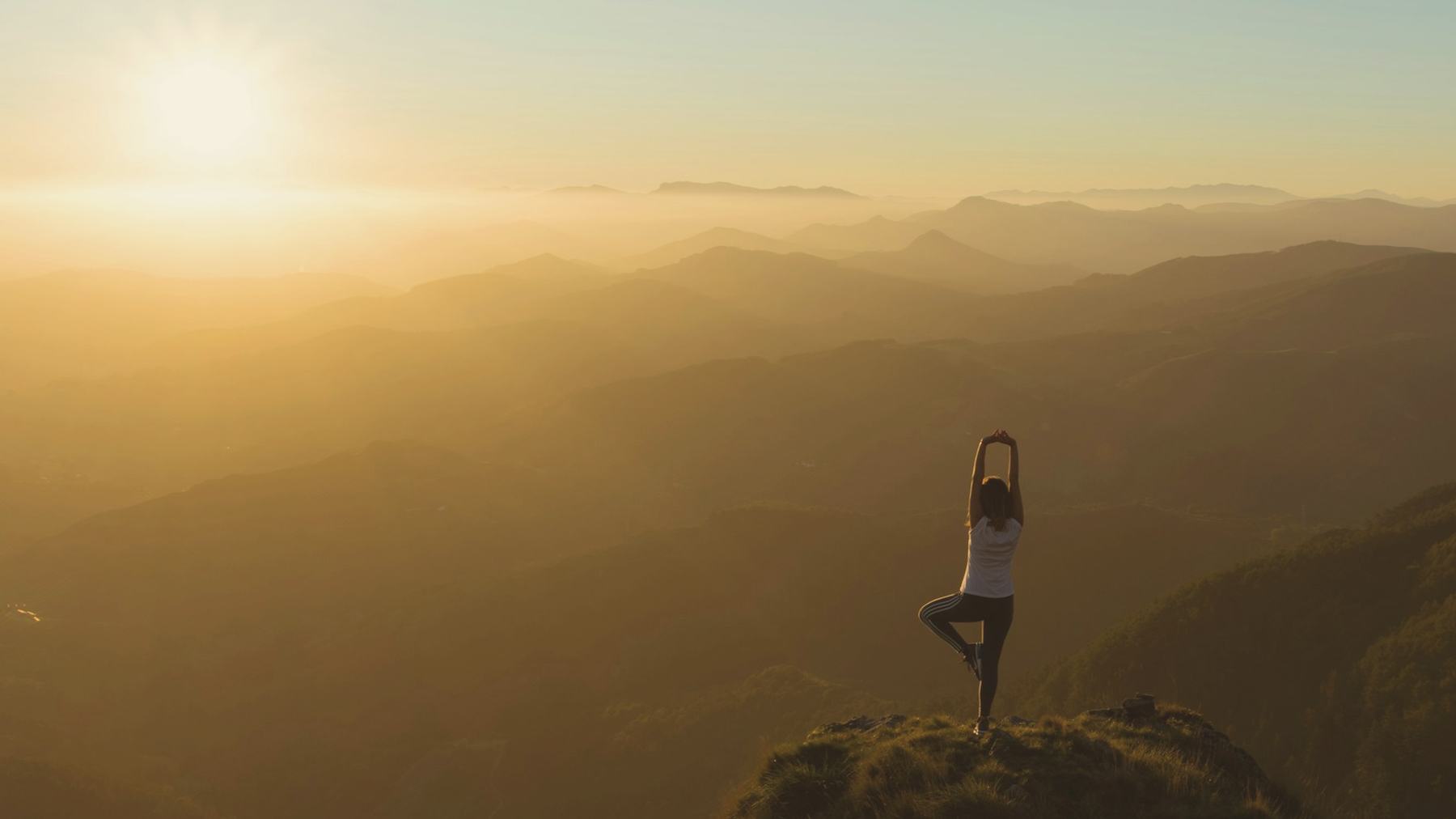 A woman in tree pose on a mountain ridge at sunrise
