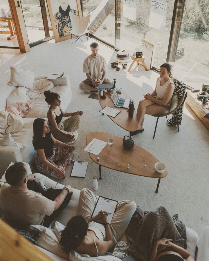 Yoga teacher trainees sitting in a circle with notebooks in a sunlit room