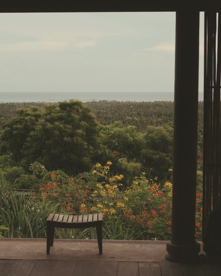 A wooden bench on a terrace looking out over a garden and the sea