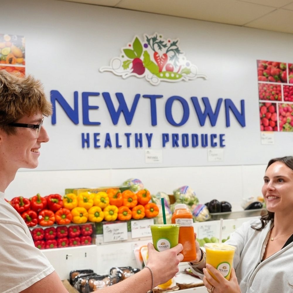 Two customers with fresh smoothies under the Newtown sign