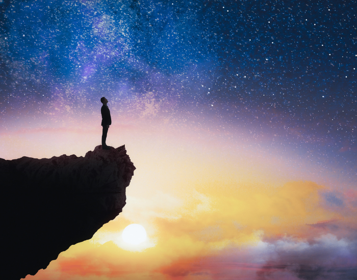 Person standing on cliff at sunset looking at the starry sky, represents person reclaiming their power and their life