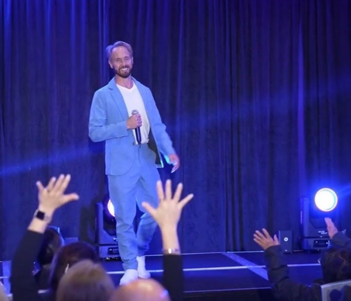 Stacey Frick speaking on stage at an event with an enthusiastic audience