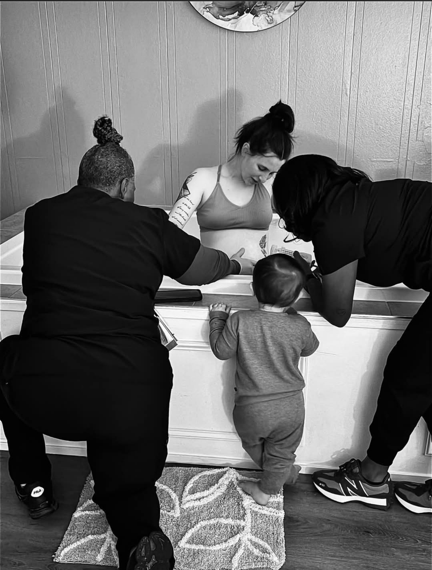 Midwife and assistant supporting a water birth, with an older sibling watching