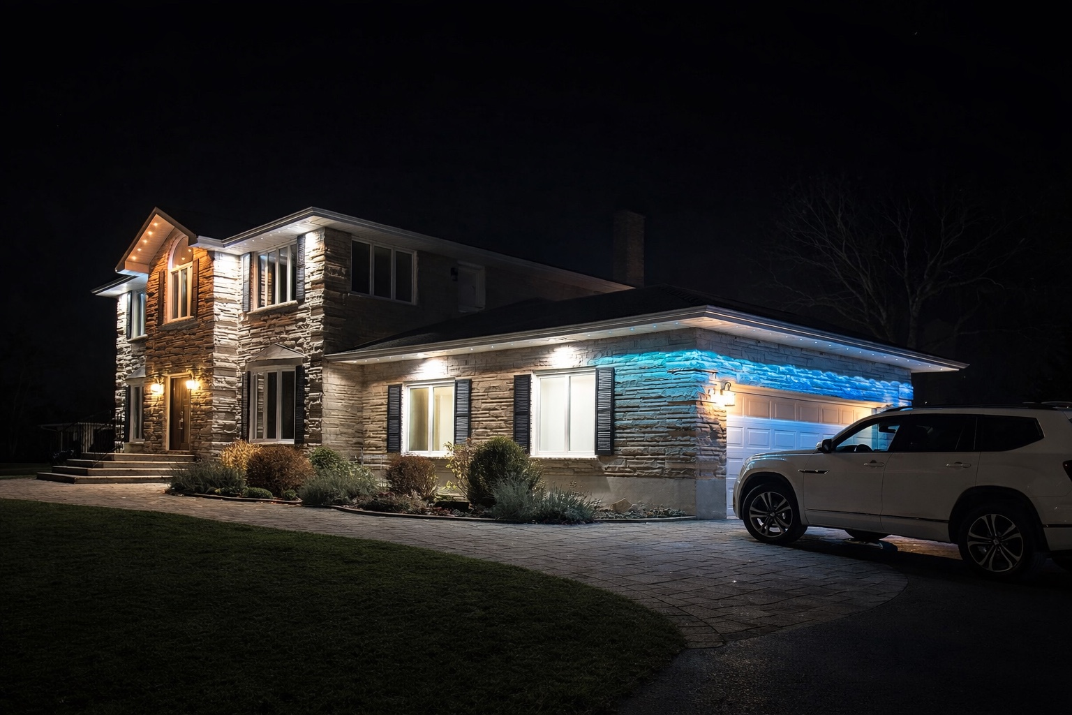 Outdoor lighting on a stone home with white roofline lights and blue colour above the garage