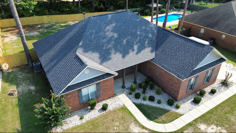 Drone photograph of completed architectural shingle roof on brick home with garage integration and American flag showing premium curb appeal