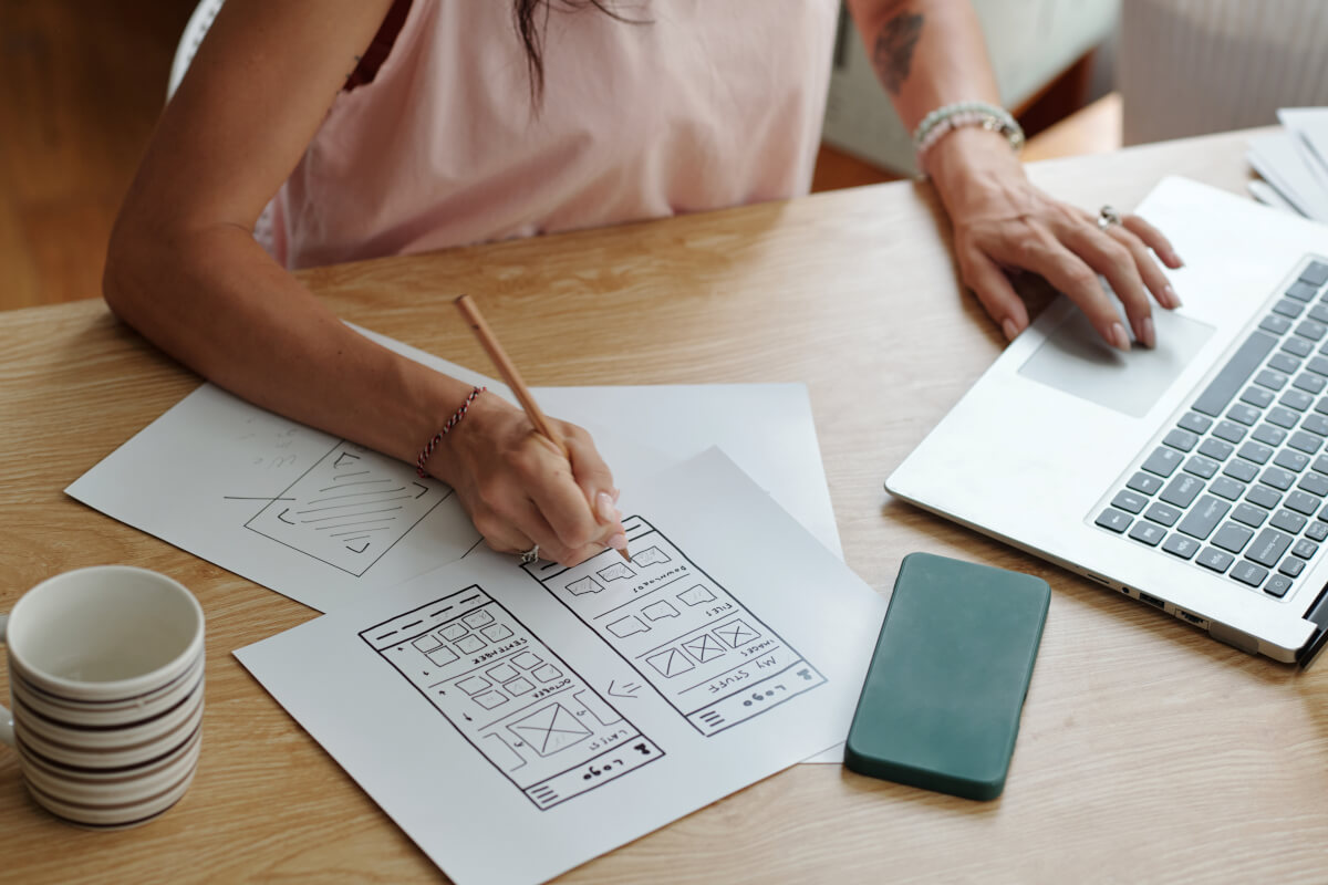 Website wireframes being sketched on paper beside a laptop