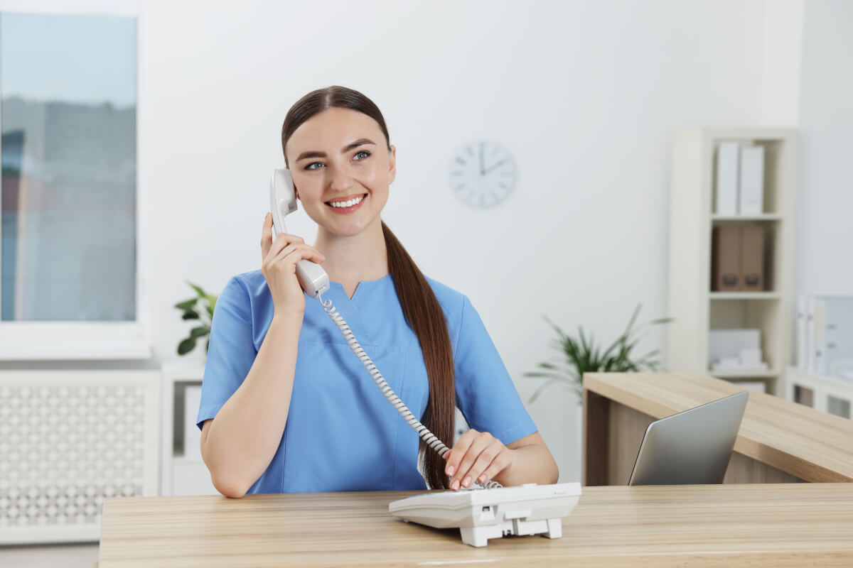 A clinic receptionist taking a call at the front desk — a person closing an inquiry
