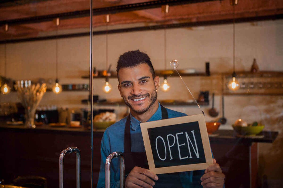 Cafe owner smiling as he turns the OPEN sign on his front door