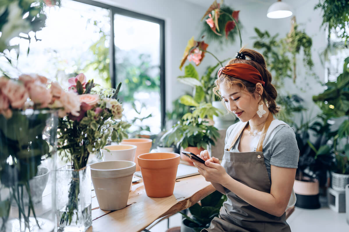 Florist checking orders on her phone at the counter of her flower shop