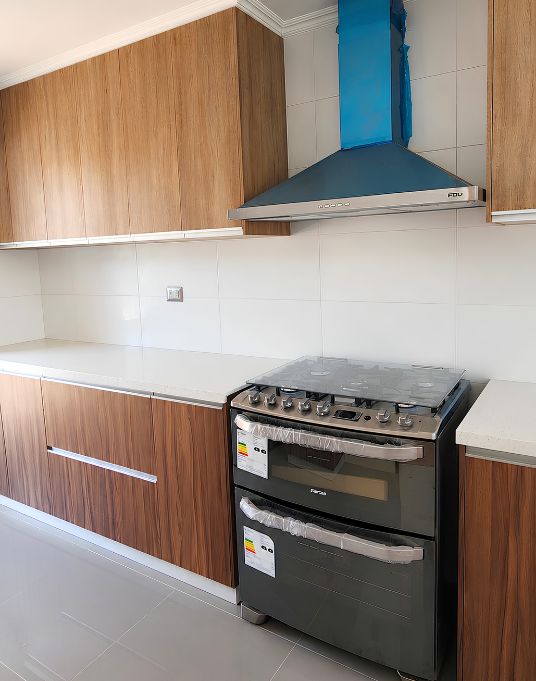 Cocina con muebles hechos a medida en tono madera, cubierta clara y campana