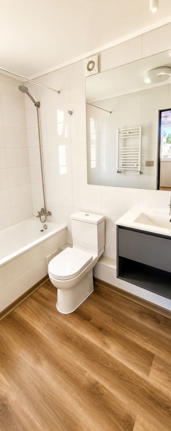 Baño remodelado con tina, revestimiento cerámico blanco, vanitorio y toallero calefactor