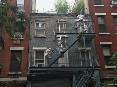 hree-story building under renovation with workers painting exterior walls in Queens