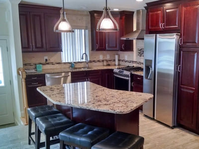 Vintage-style kitchen renovation in Queens featuring dark wood cabinets, granite countertops, and a kitchen island with bar stools.