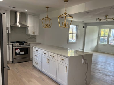 Bright white kitchen with a large island, gold pendant lighting, and stainless steel appliances.