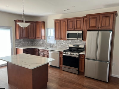 Modern kitchen renovation featuring brown wood cabinets, stainless steel appliances, and a central island.