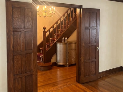 Beautifully crafted wooden staircase and hallway with rich wooden doors and chandelier lighting.