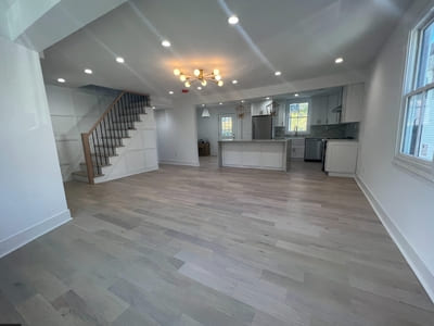 Open-concept living area and modern kitchen with light wood flooring, a stylish staircase, and recessed lighting.