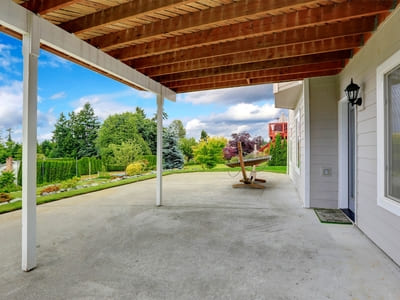 Spacious backyard patio with a concrete floor under a wooden deck, overlooking a landscaped garden.