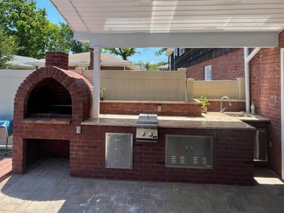 Outdoor brick kitchen with a built-in pizza oven and stainless steel appliances, perfect for backyard entertaining.