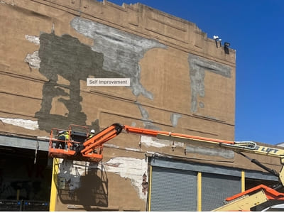 Building facade repair in progress with workers on a lift applying concrete to damaged areas.