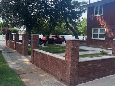 Brick fence installation around a residential property with sturdy pillars and a landscaped garden.