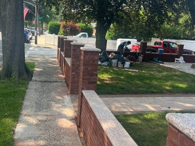 Side view of brick fence installation in Brooklyn, with workers completing landscaping work inside the fenced area.