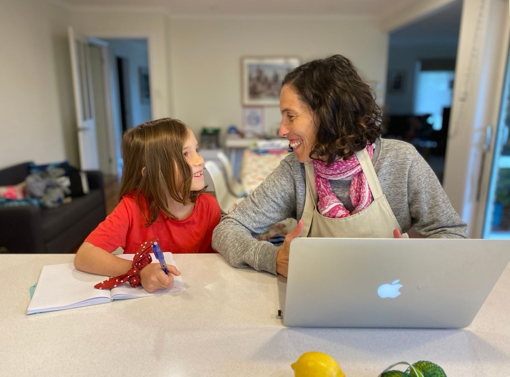 A mother and daughter laughing together over homework at the kitchen table