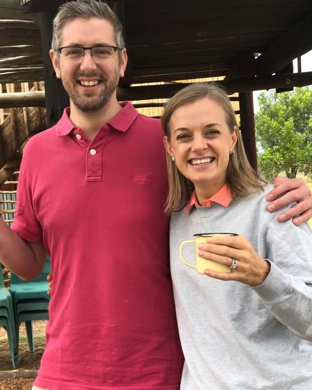 Magnus and Lenise smiling outdoors, each holding an enamel mug